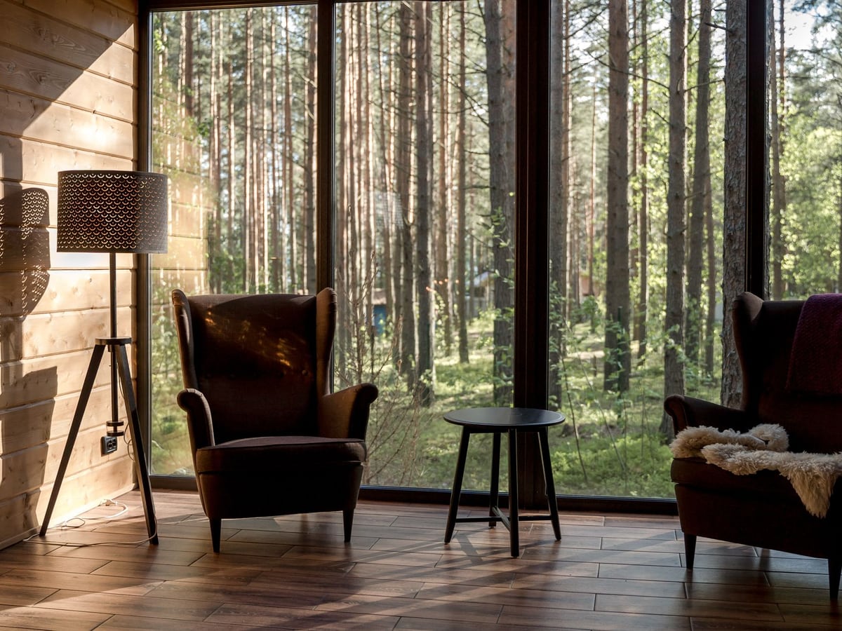 Coin salon de chalet en bois avec lampadaire allumé face à une forêt de pins