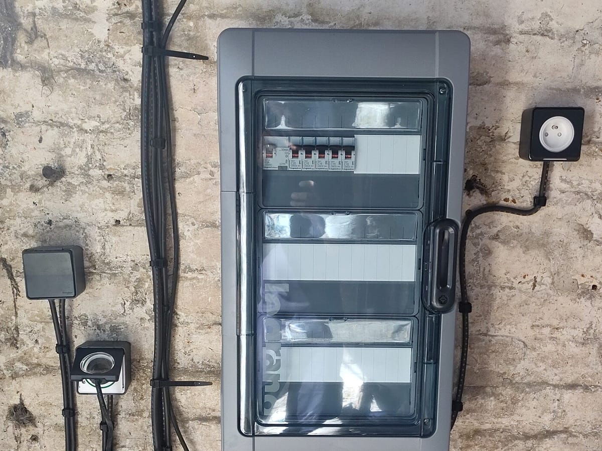 Coffret électrique étanche neuf et prises posés sur un mur en pierre ancien
