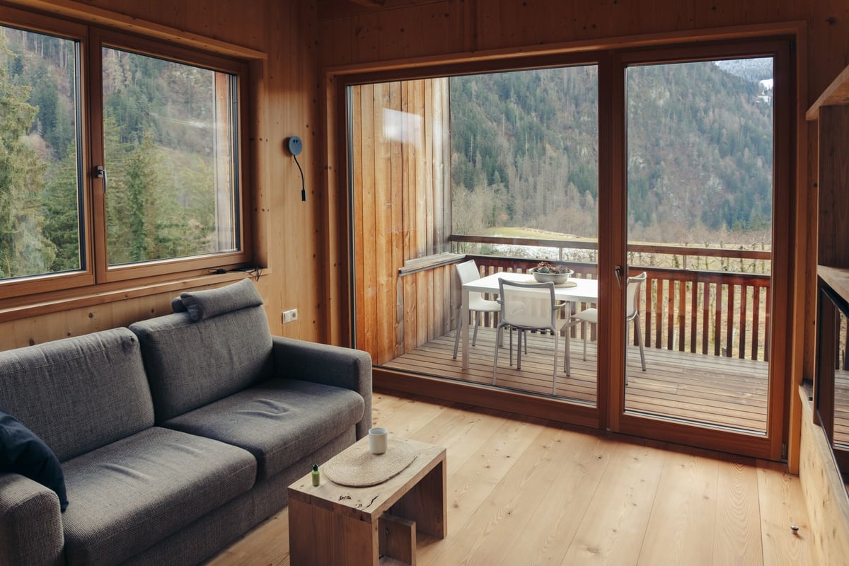Séjour de chalet en bois clair ouvert sur un balcon et la forêt de montagne